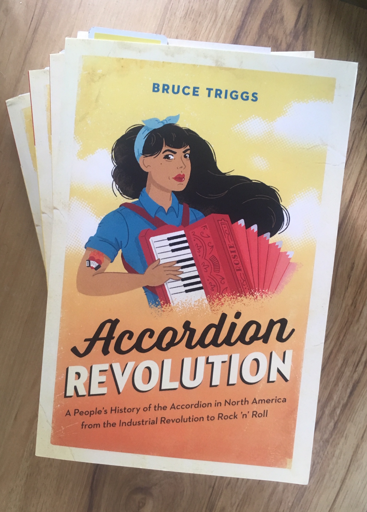 A stack of four copies of Accordion Revolution, on a woodgrain background